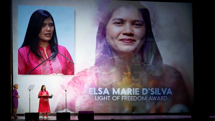 Woman in red stands at awards podium in front of a large picture of herself