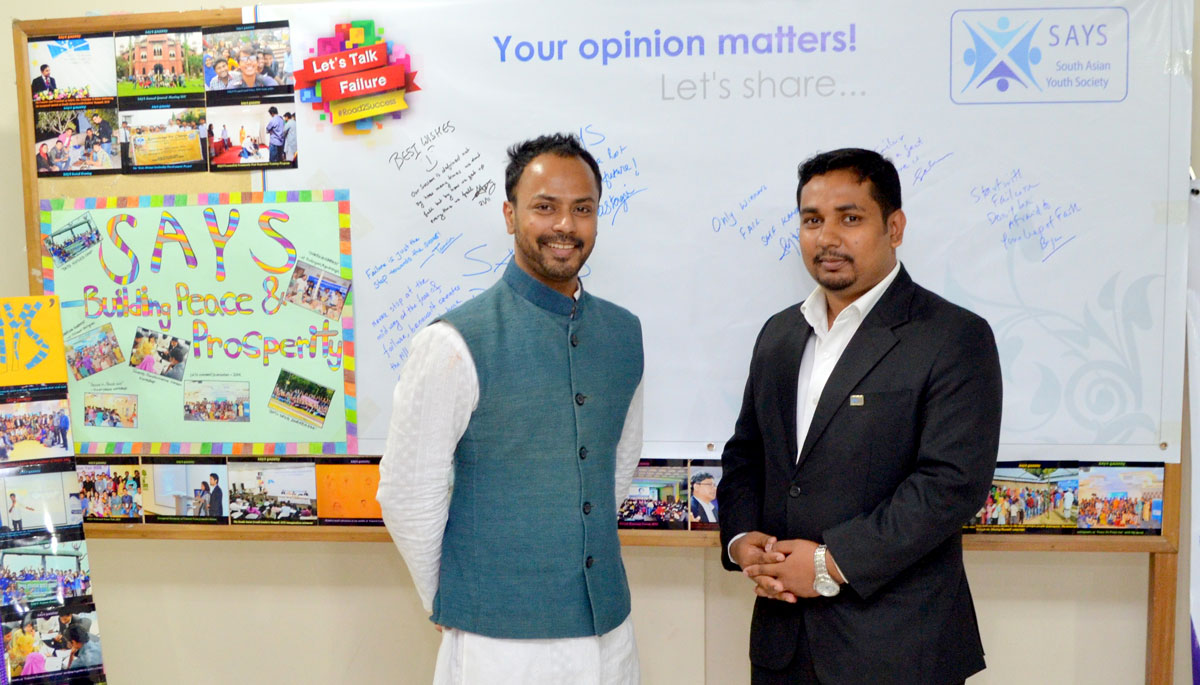 Two men standing in classroom with posters and writing on board behind them