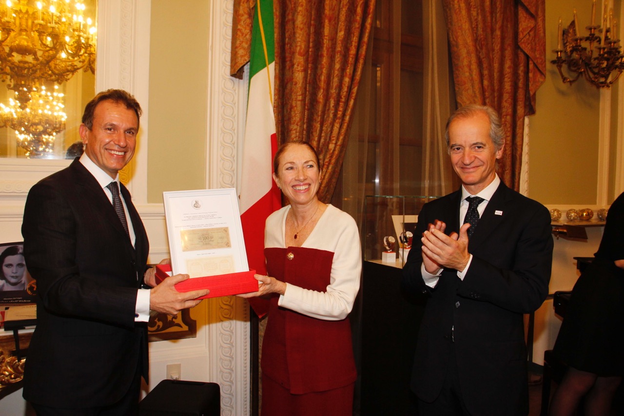 Woman receiving award with a big smile from man handing it to her and others stand around clapping