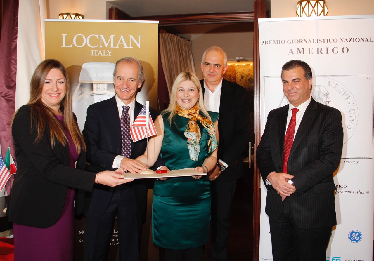 Three men and two women stand passing an award and American flag with smiles