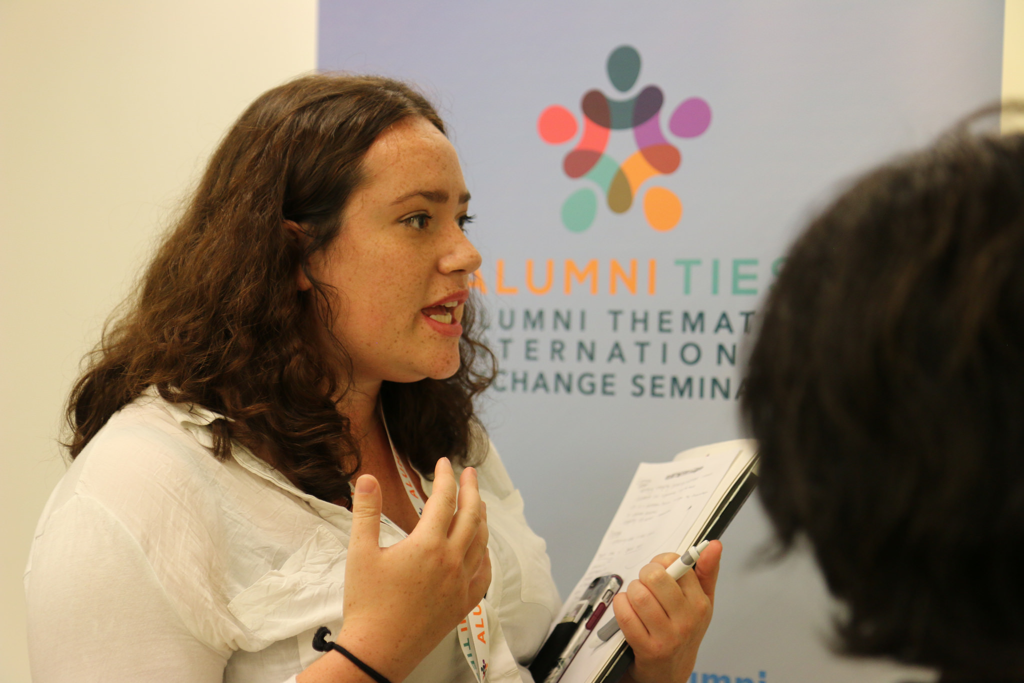 Woman talking with notepad in her hand and TIES logo on wall in background