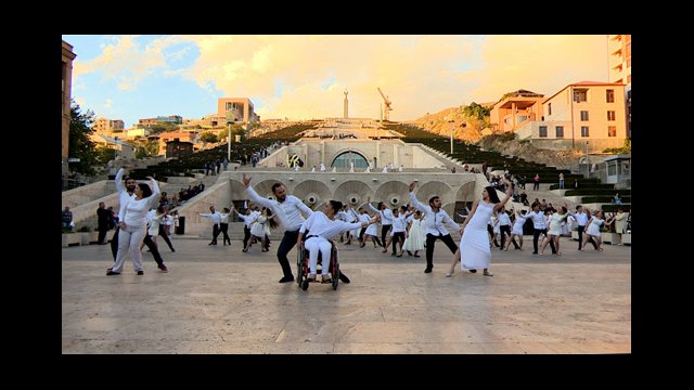 Armenian dancers dance in formation in front of grand stairs 