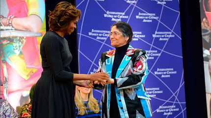 Older woman in colorful jacket shakes hands with former First Lady Michelle Obama