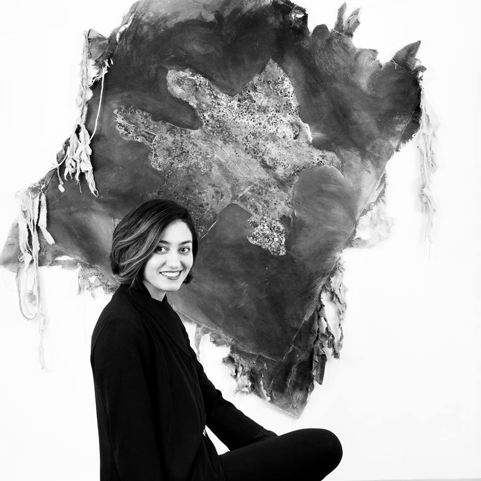 Woman smiling in front of a hanging textile art piece