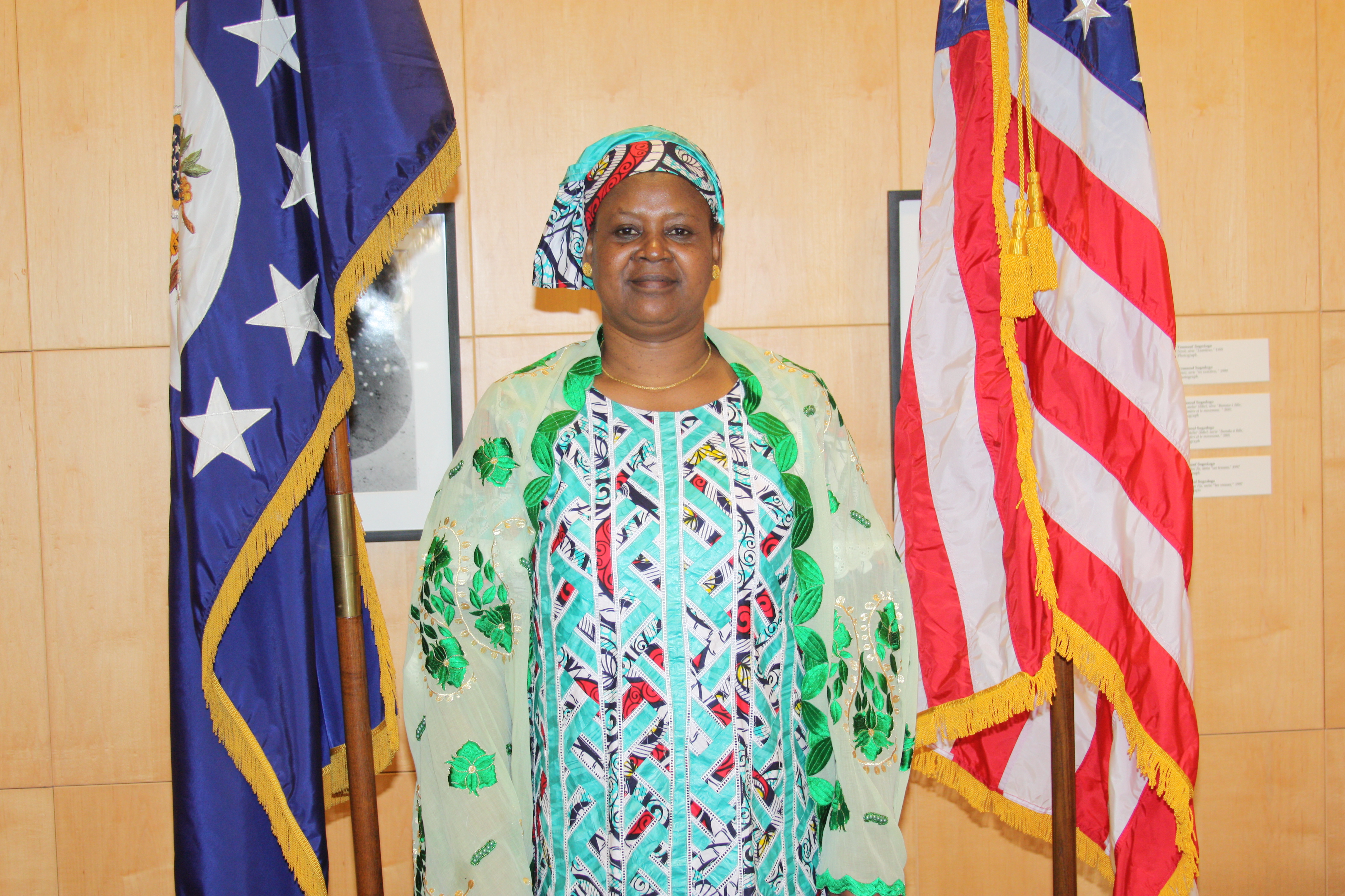 Women dressed in African print attire stands between American flag and unknown other flag