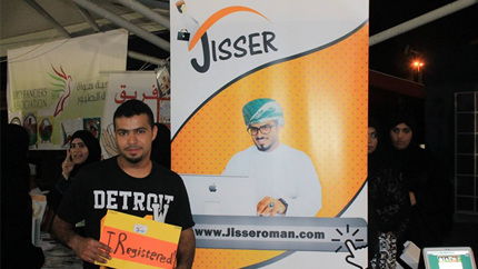 Student stands in front of a promotional banner for the Jisser website, holding a sign indicating he registered for the site