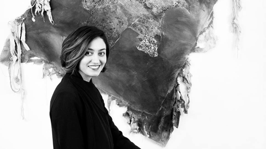 Woman smiling in front of a hanging textile art piece