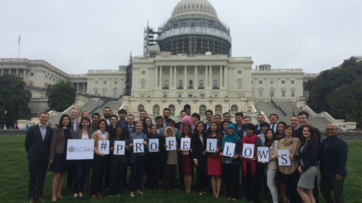 People posing in front of the U.S. Capitol building holding signs that spell out "#PROFELLOWS"