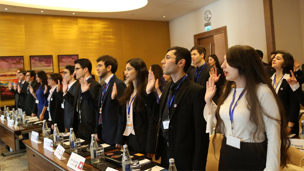 Group of professionally dressed young people holding up their right hands as if taking an oath.