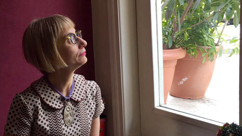 Woman with short hair and wearing glasses looks out of a window