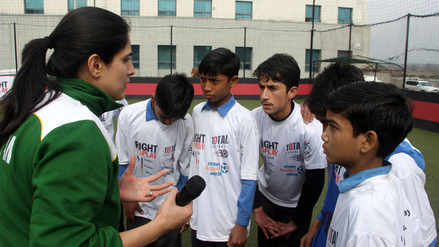 Woman standing in front of a small group of boys holding a basketball