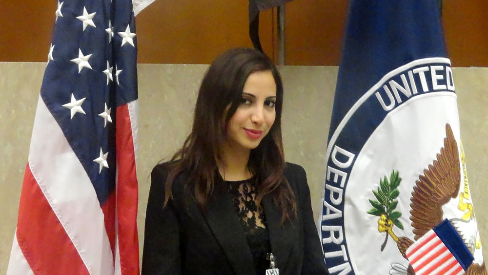 Young woman standing between the U.S. flag and Department of State flag