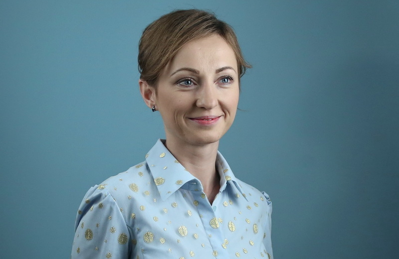 Smiling young woman with short blonde hair wearing a blue collared shirt 