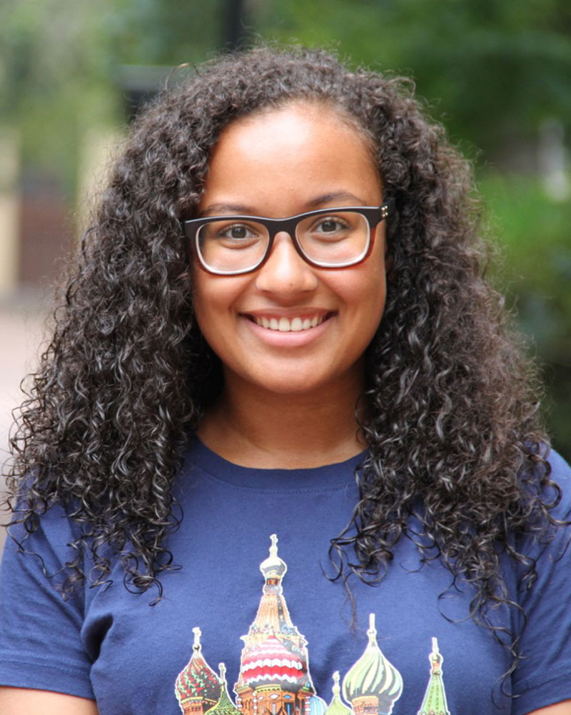 Young lady with long curly hair wearing glasses and smiling