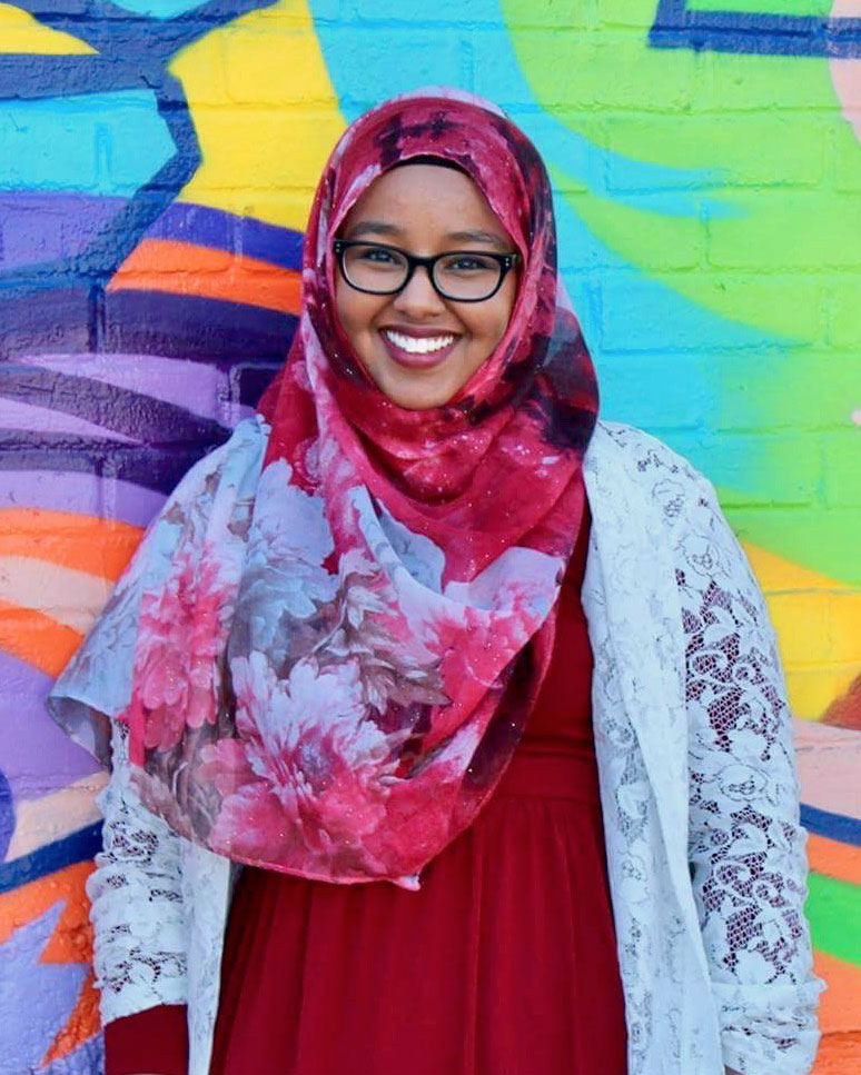 Young lady with head wrap stands against colorful wall