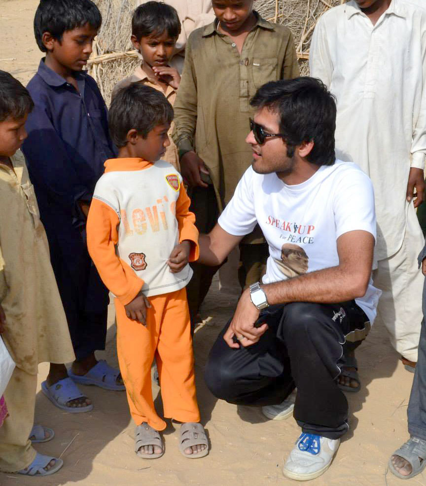 Young man kneels down to talk with small boy as other young boys surrounding them observe