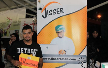 Student stands in front of a promotional banner for the Jisser website, holding a sign indicating he registered for the site
