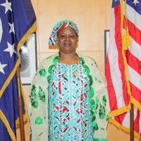 Women dressed in African print attire stands between American flag and unknown other flag