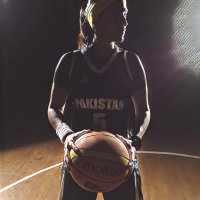 Dimly lit women holding basketball and standing on a basketball court in basketball uniform