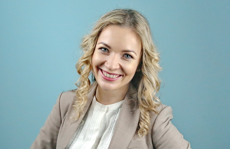 Young smiling Ukrainian woman with shoulder-length curly blond hair in beige blazer over a white nehru collared shirt.